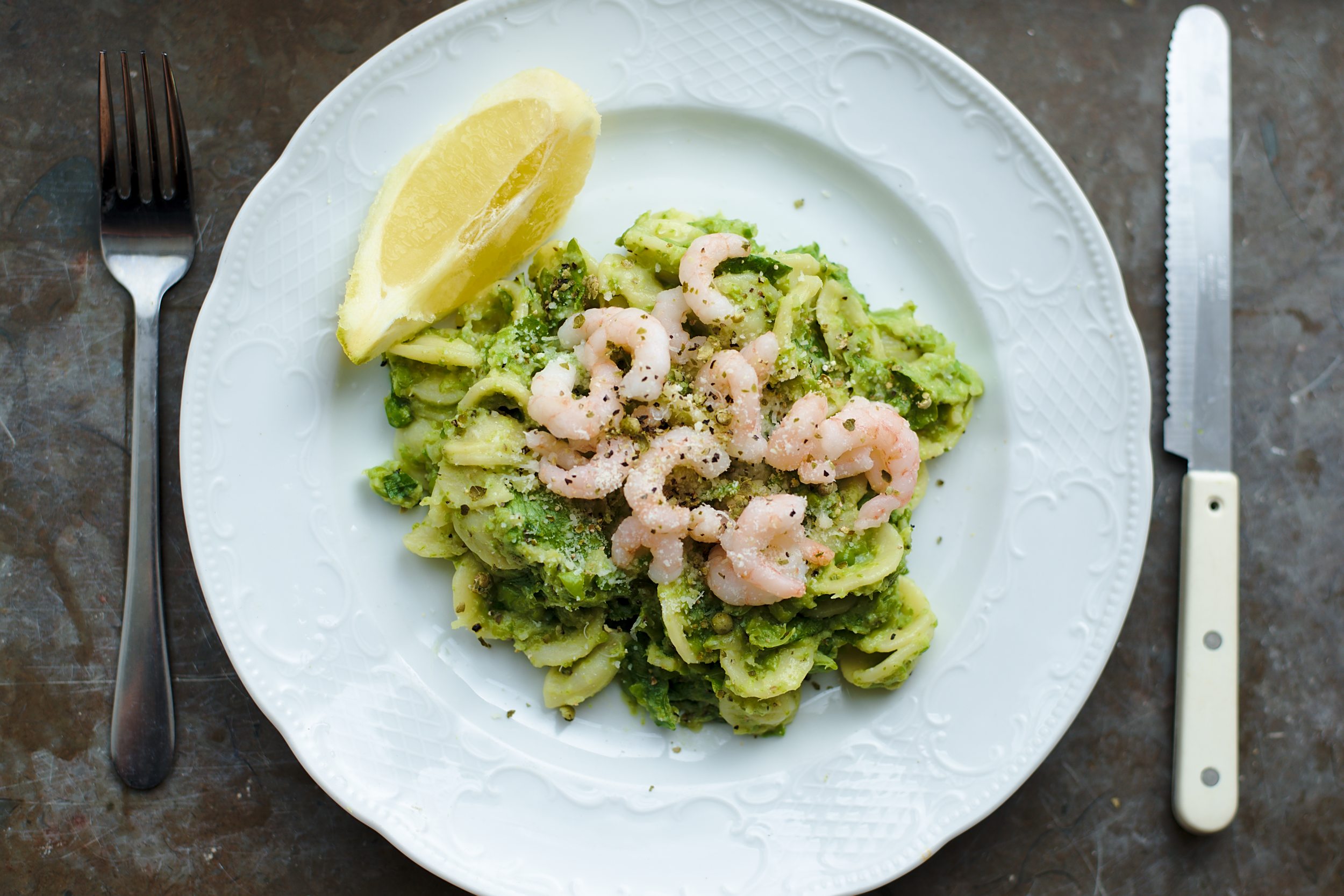 Orecchiettepasta with green pea pesto and prawns on a white plate