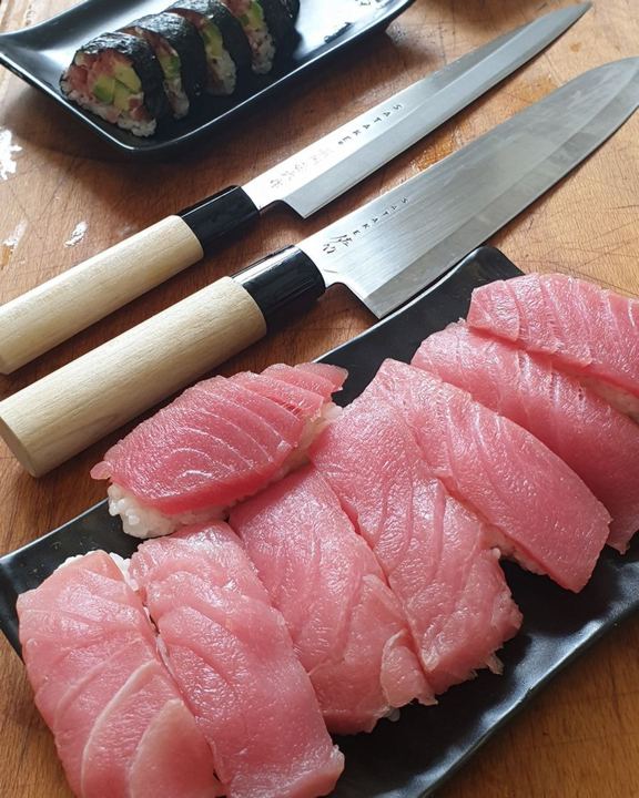 ten tuna nigiri and rolls in the background, japanese knifes in between