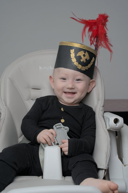 Baby with coal miner hat on gray chair