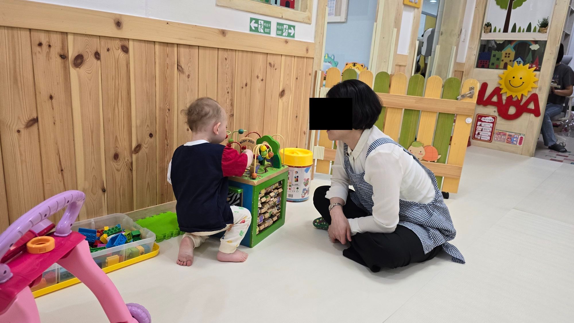 Boy plying with toys at daycare, teacher looking at him